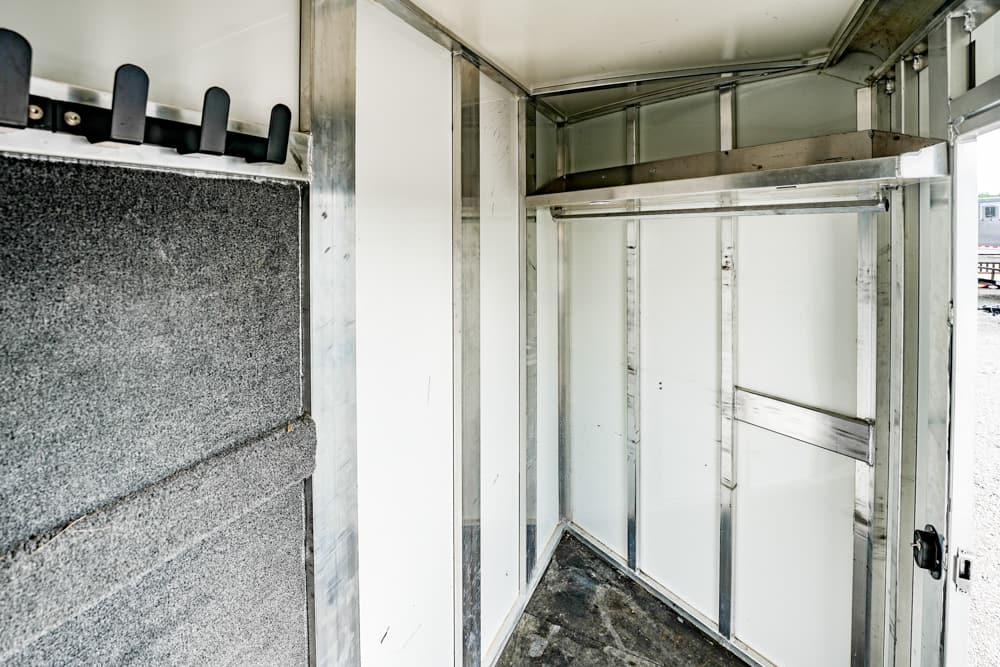 Interior of a metal transport trailer: white walls, exposed framing, and a top storage shelf.