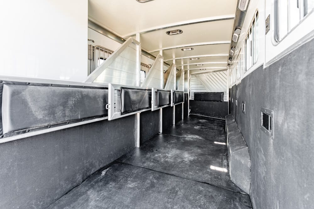 Interior of a horse trailer showing row of divider stalls and dark rubber-lined walls.
