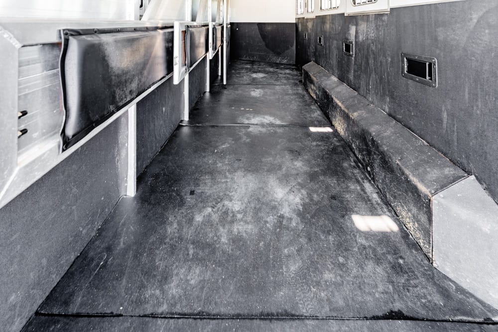 Empty cargo trailer interior with black rubber floor and side storage compartments along the walls, viewed toward the rear.