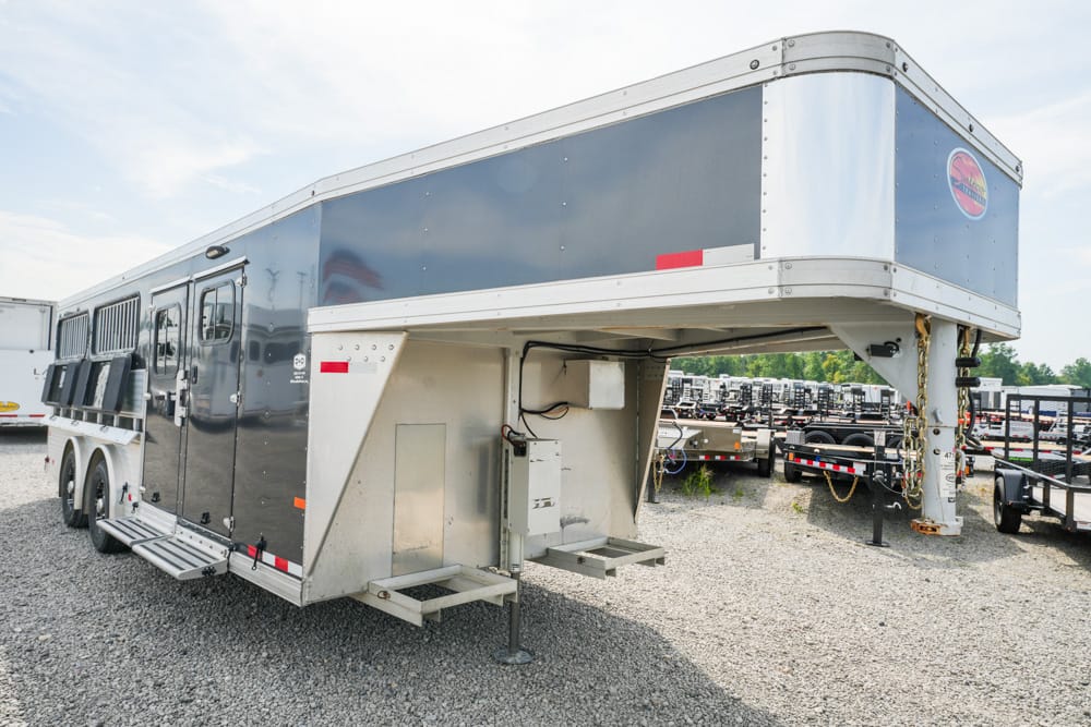 Gooseneck horse trailer with a raised front living quarters section parked on a gravel lot; other trailers visible in the background.