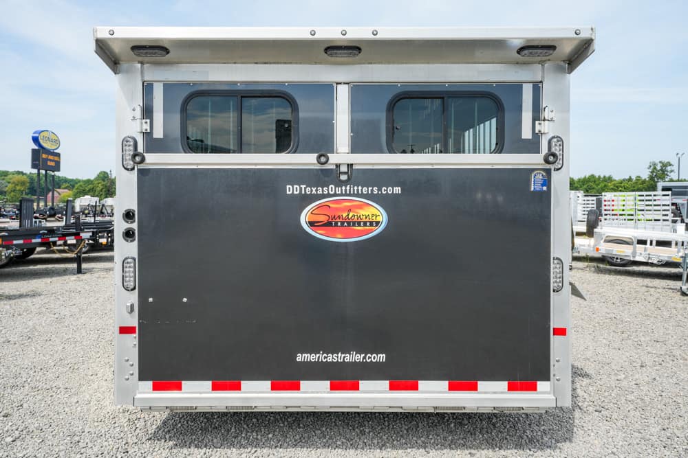 Rear view of a black Sundowner trailer door with brand logos and two small windows above, on a gravel lot