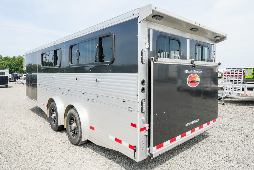 Two-tone aluminum horse trailer with dark blue upper section and windows along the side, parked on a gravel lot.