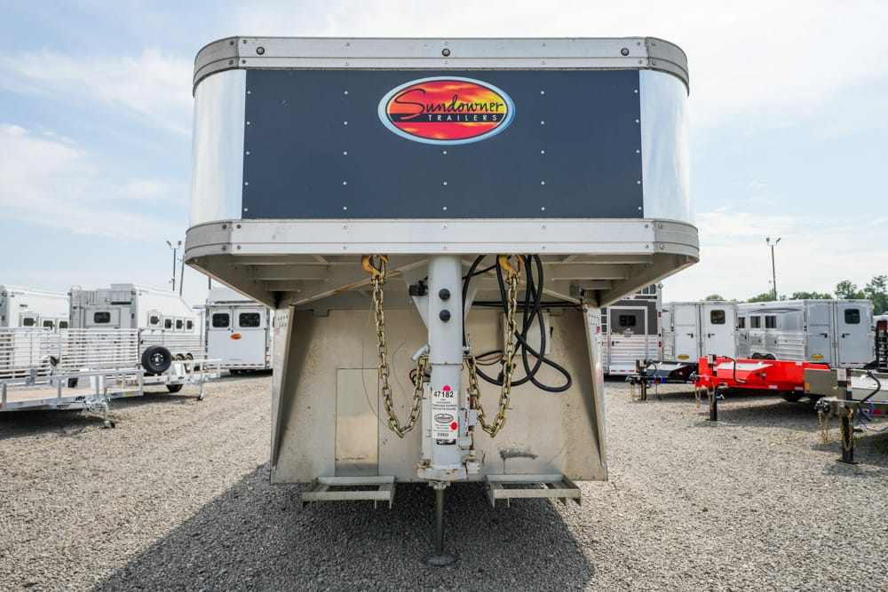Front view of a Sundowner gooseneck trailer in a gravel lot, with other trailers in the background and the logo visible on its nose.