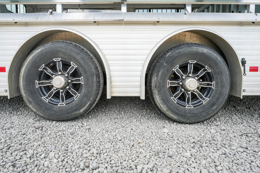 Side view of a white trailer with dual axles and large black tires on gravel ground to the left and right of the frame.