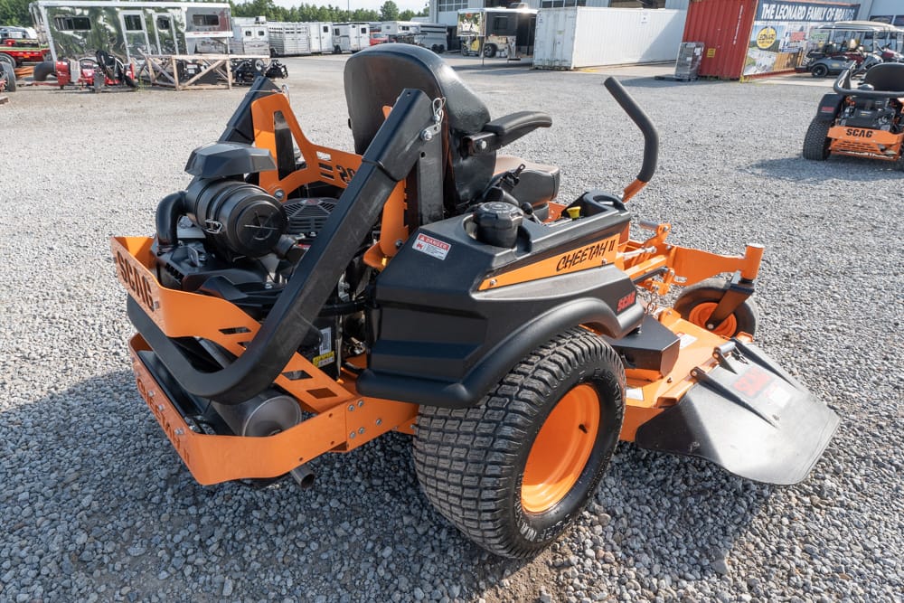 Orange SCAG Cheeta II zero-turn mower with black seat and dual control levers parked on a gravel lot at a equipment yard.