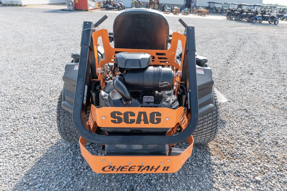 Back view of an orange and black SCAG Cheetah II riding mower on a gravel lot, showing the engine and roll bars behind the seat at center stage.