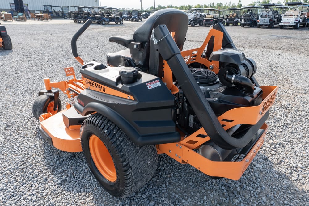 Orange and black Cheetah II ride-on mower on a gravel lot, with safety roll bar visible in the background] ,