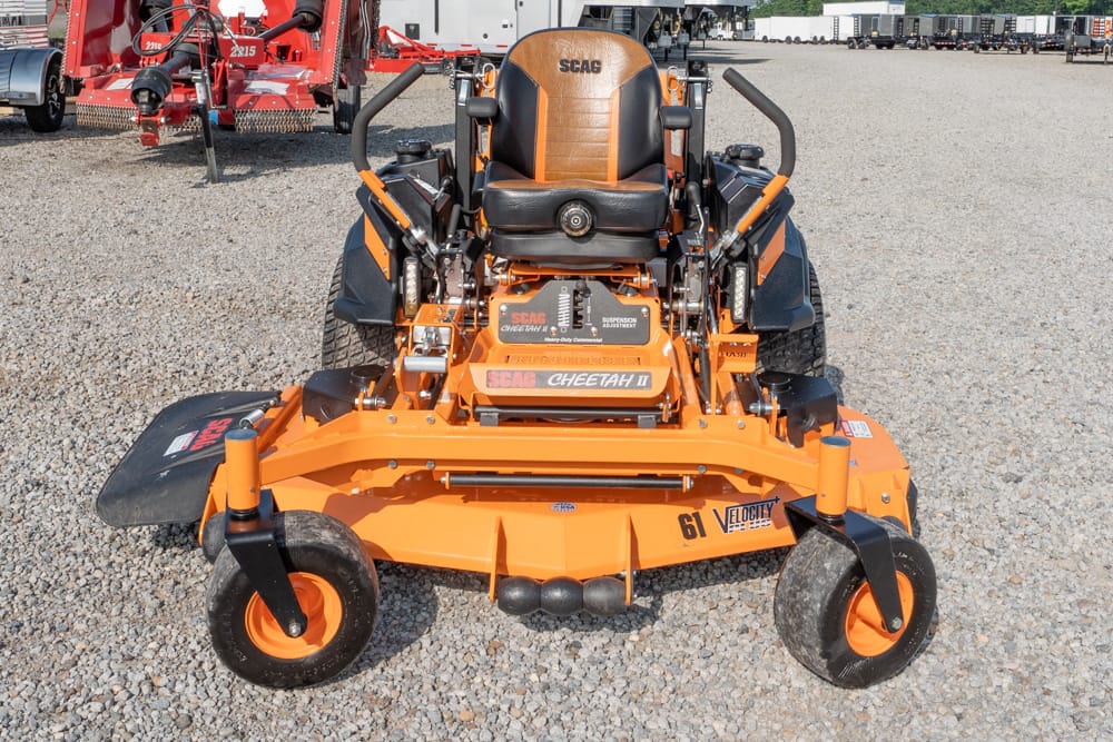 Front view of an orange SCAG Cheetah II zero-turn lawn mower on a gravel lot, showing the big seat and dual control levers.