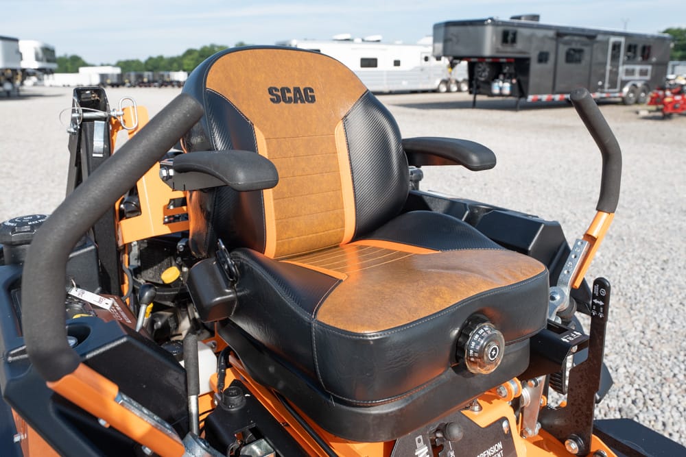 Close-up of an orange and black SCAG riding mower seat on a lawn tractor with controls visible nearby.