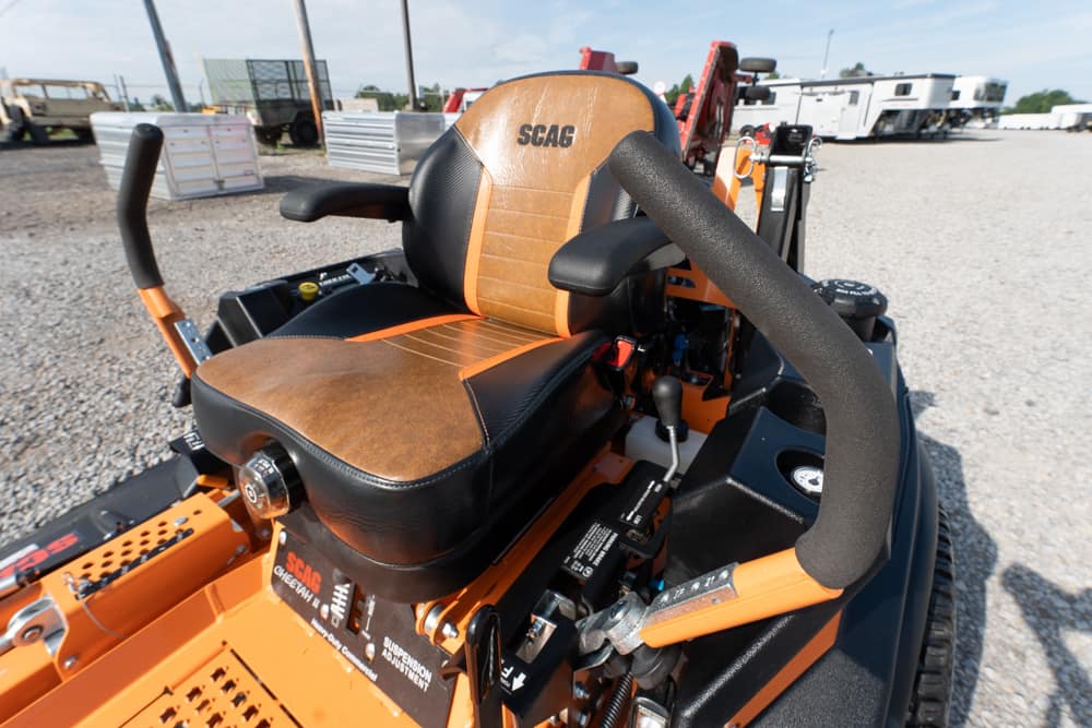SCAG ride-on lawn mower seat in orange and black, with armrests and controls on a gravel lot
