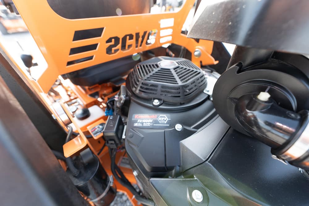 Close-up of an orange heavy equipment interior showing a black Kawasaki engine and cooling fan assembly behind it