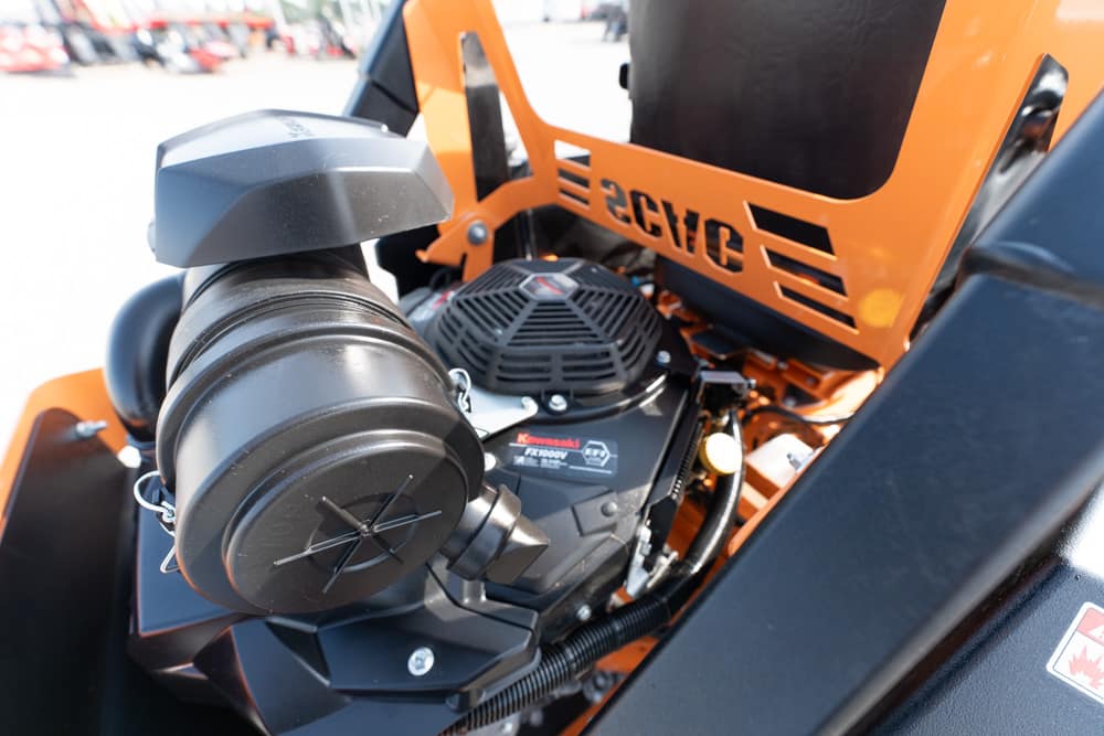 Close-up of an orange industrial machine's engine area, showing a black round air-filter housing and surrounding components.
