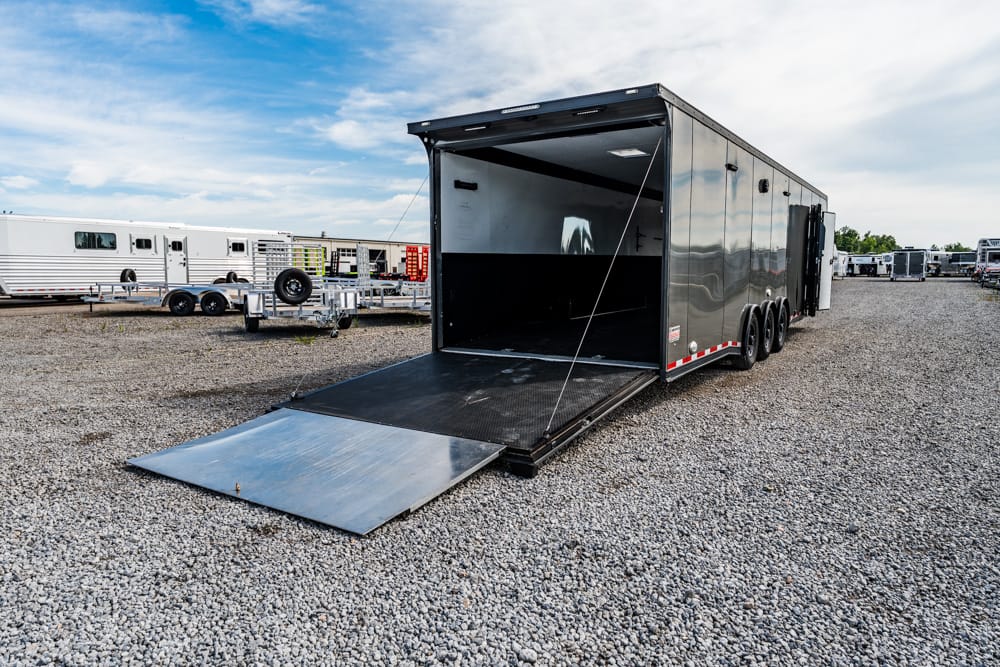 Enclosed black cargo trailer with its loading ramp down on a gravel lot, other trailers in the background