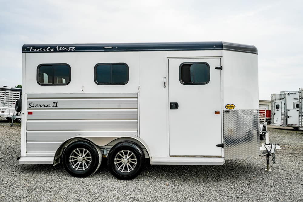White Trails West Sierra II horse trailer with two side windows and a front door on a gravel lot, dual-axle wheels visible.