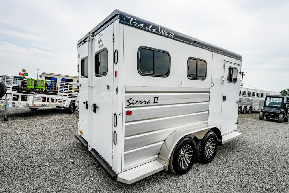 White Trails West Sierra II horse trailer with dual axles parked on gravel lot, side branding visible.