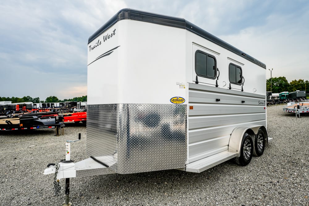White tandem-axle travel trailer with diamond-plate front, parked on a gravel lot