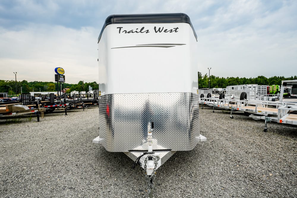 Front view of a Trails West trailer with a diamond-plate nose parked on a gravel lot near other trailers.