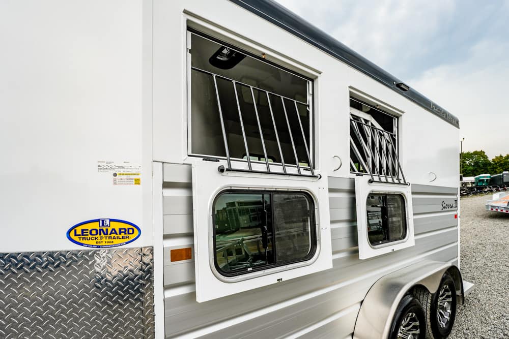 White horse trailer with two open, barred windows and a Leonard trailer sticker on the side.