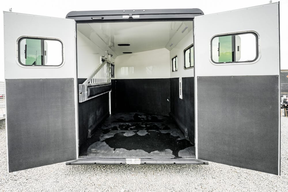 Open horse trailer interior with a partition on the left and windows along the walls; the stall is empty and the floor has dark patches.