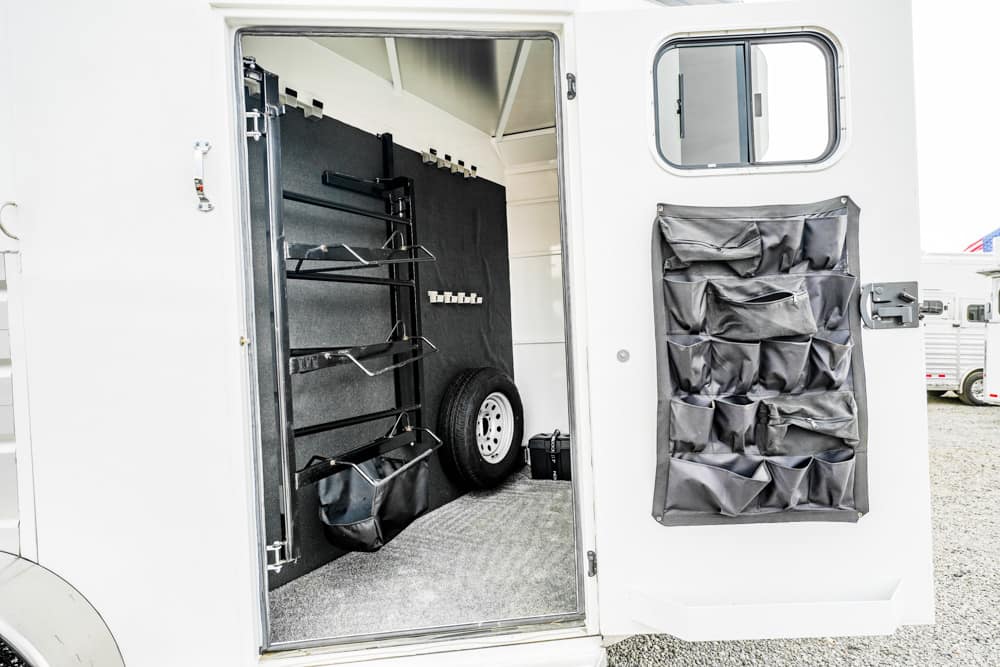 Open trailer cargo area showing a vertical rack system, shelves, a spare tire, and a hanging fabric organizer on the door.