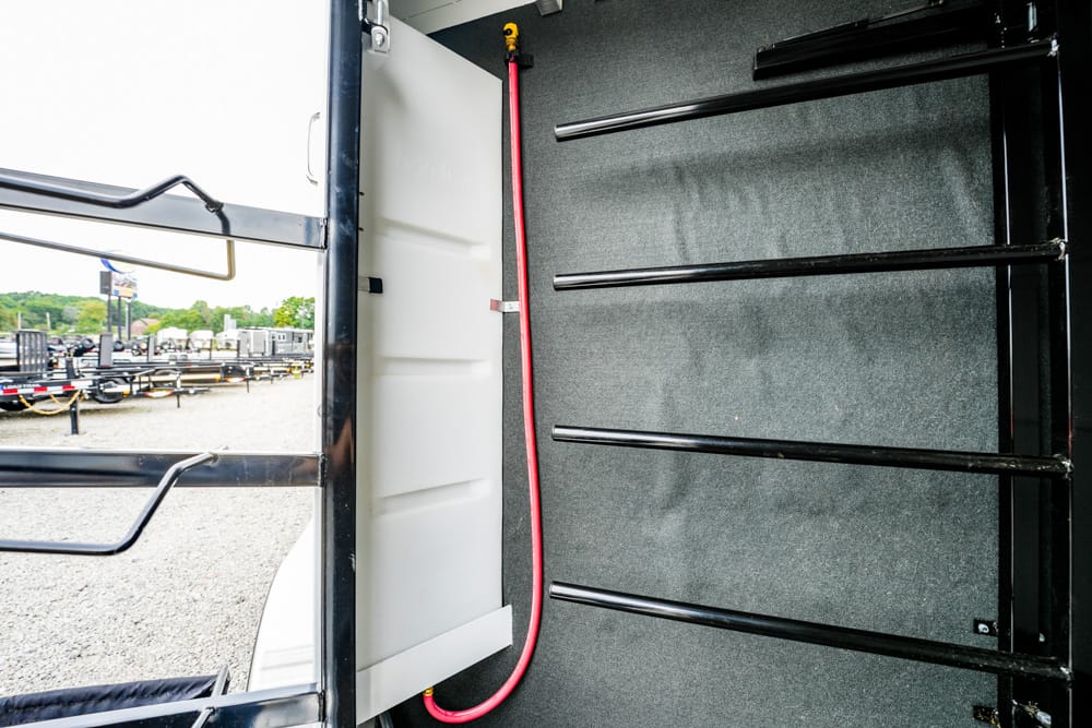 Interior of a trailer showing black ladder-style racks on the right and a red power cord along the wall; outdoor lot with more trailers visible through the open door.