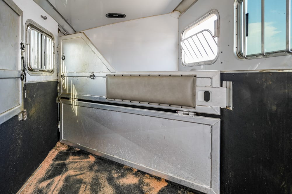 Interior of a metal animal trailer with a padded stall divider and sliding partition, white walls and small windows with bars.
