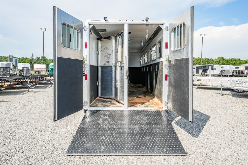 Open horse trailer with a lowered ramp revealing an empty interior and rust on the floor.
