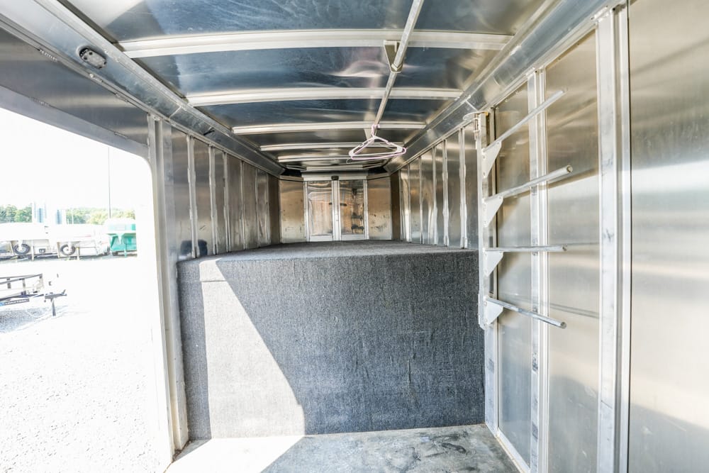 Interior of an empty metal trailer with a gray divider and overhead hooks, ready for transporting equipment or animals.