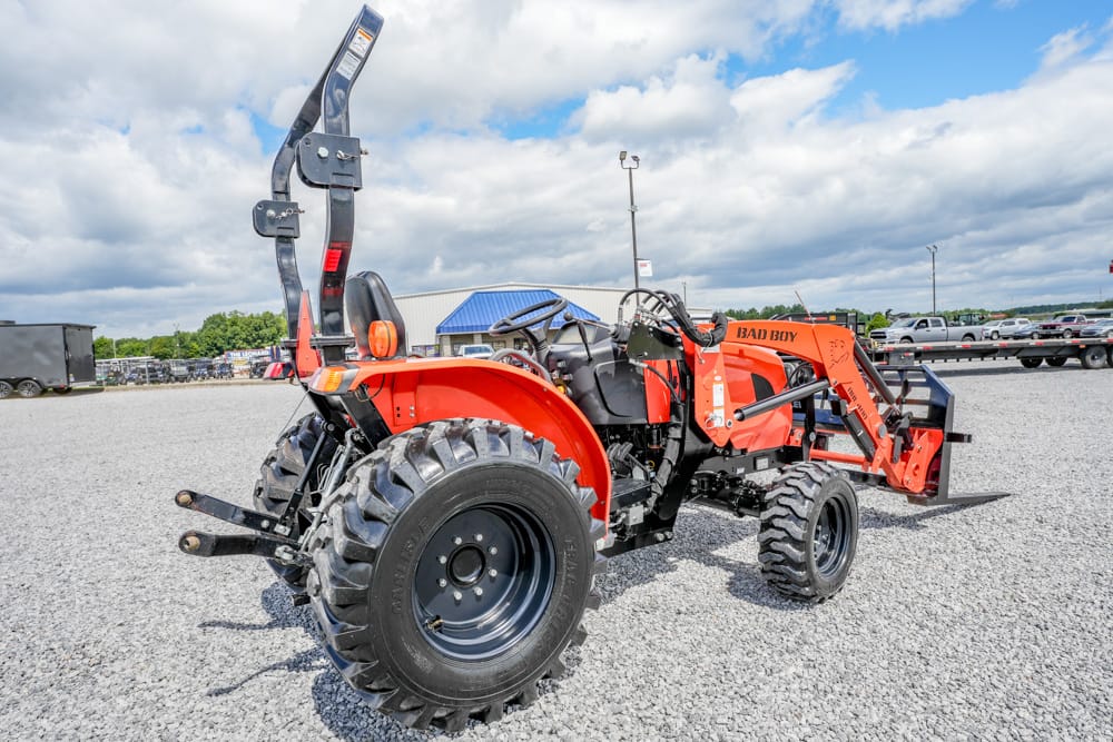 Red Bad Boy compact utility tractor with front loader raised, parked on a gravel lot.