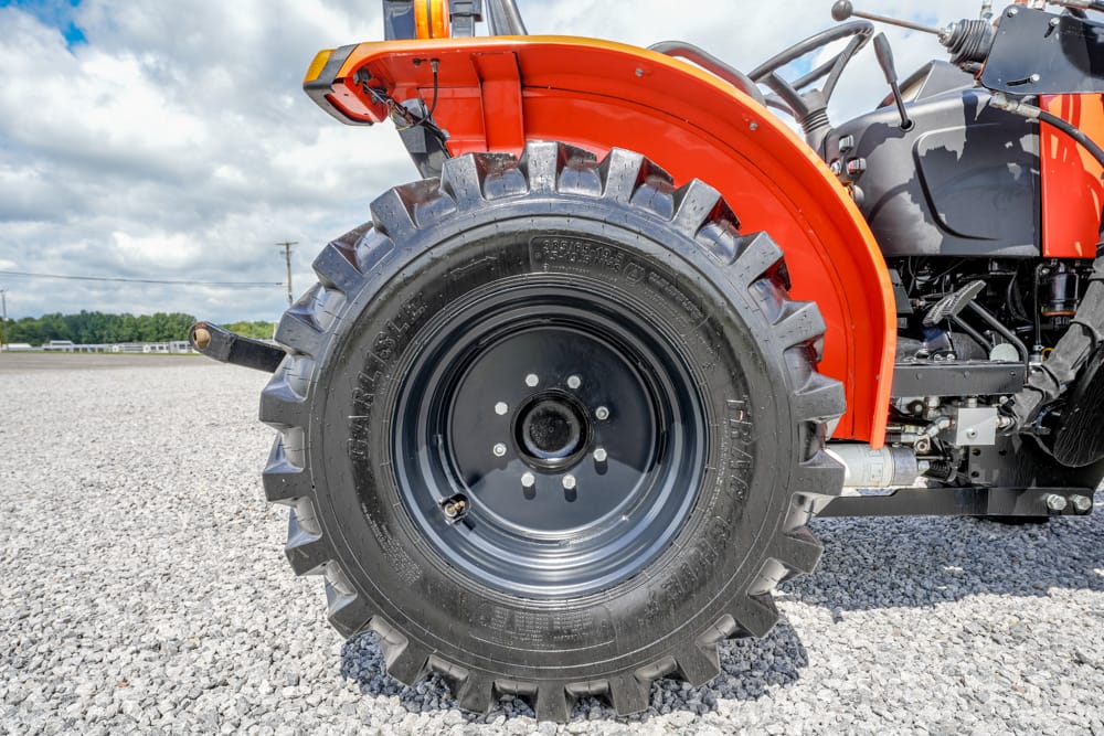 Close-up of a large rugged tractor tire with a red fender on a gravel lot.