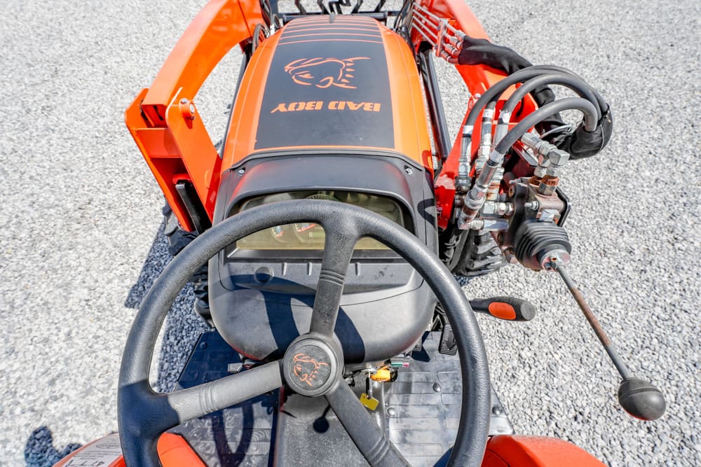 Top-down view of an orange tractor cockpit with steering wheel, dashboard, and hydraulic control levers on the right.
