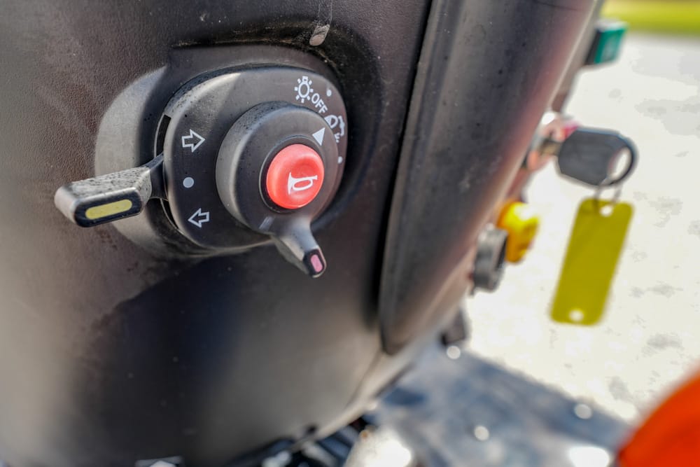 Close-up of a red emergency stop button on a vehicle dashboard, with a key and yellow tag in the background.