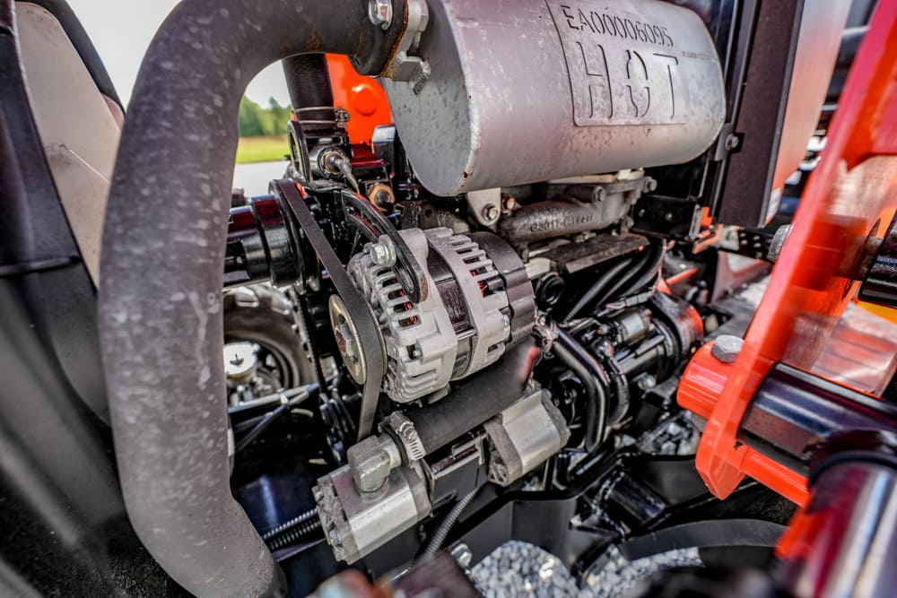 Close-up of a tractor engine showing an alternator, belts, and red frame components.