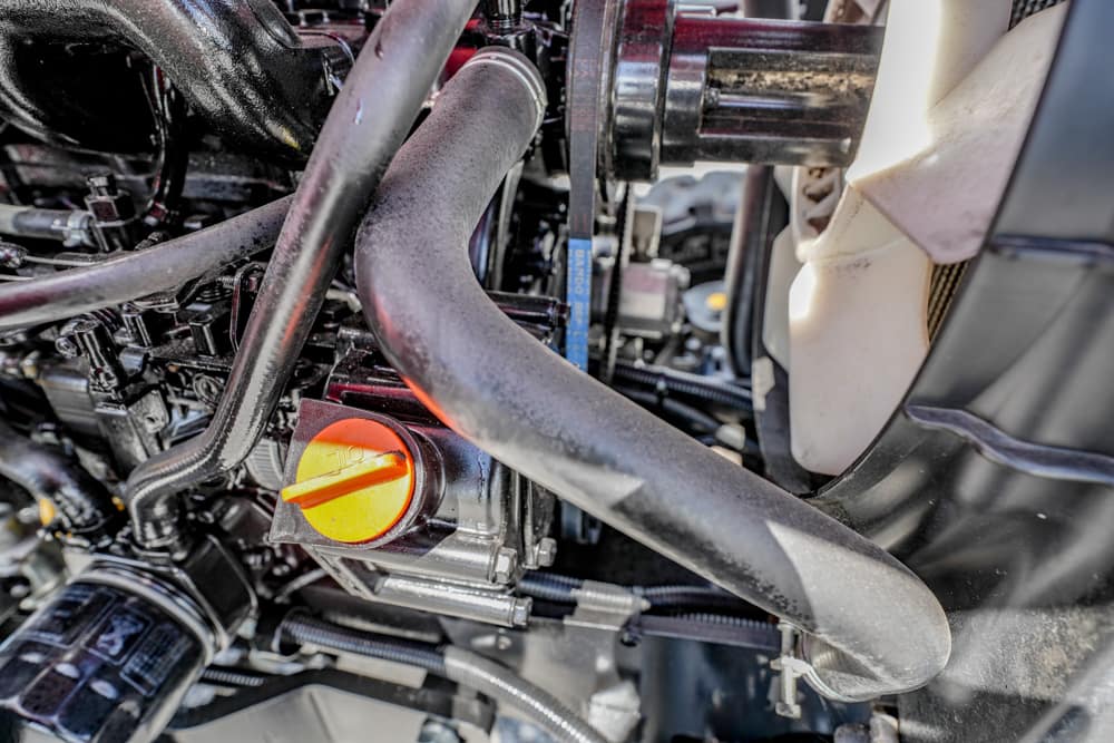 Close-up of a car engine bay showing a bright orange oil dipstick knob among black hoses and metal components.
