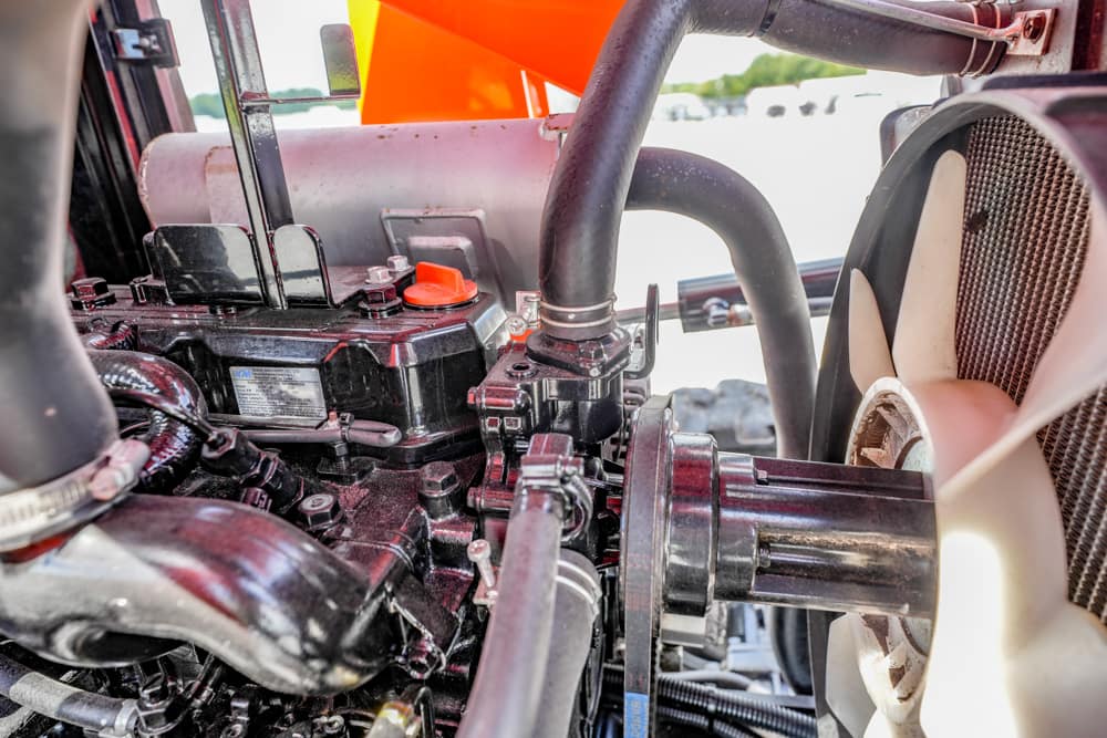 Close-up of a construction vehicle engine showing belts, hoses, and a large cooling fan on the right side.