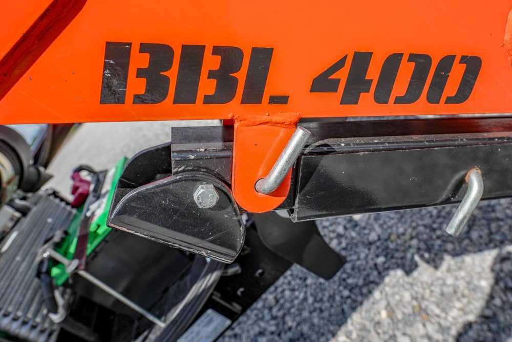 Close-up of an orange vehicle/frame with bold black numbers '1331.400' and a metal hitch/attachment hooks at the bottom right corner revealing part of a green component nearby.