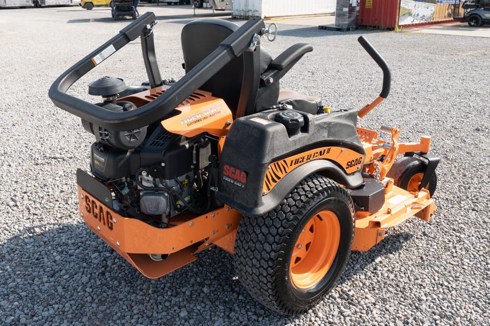 Orange SCAG riding lawn mower with black seat on a gravel surface.