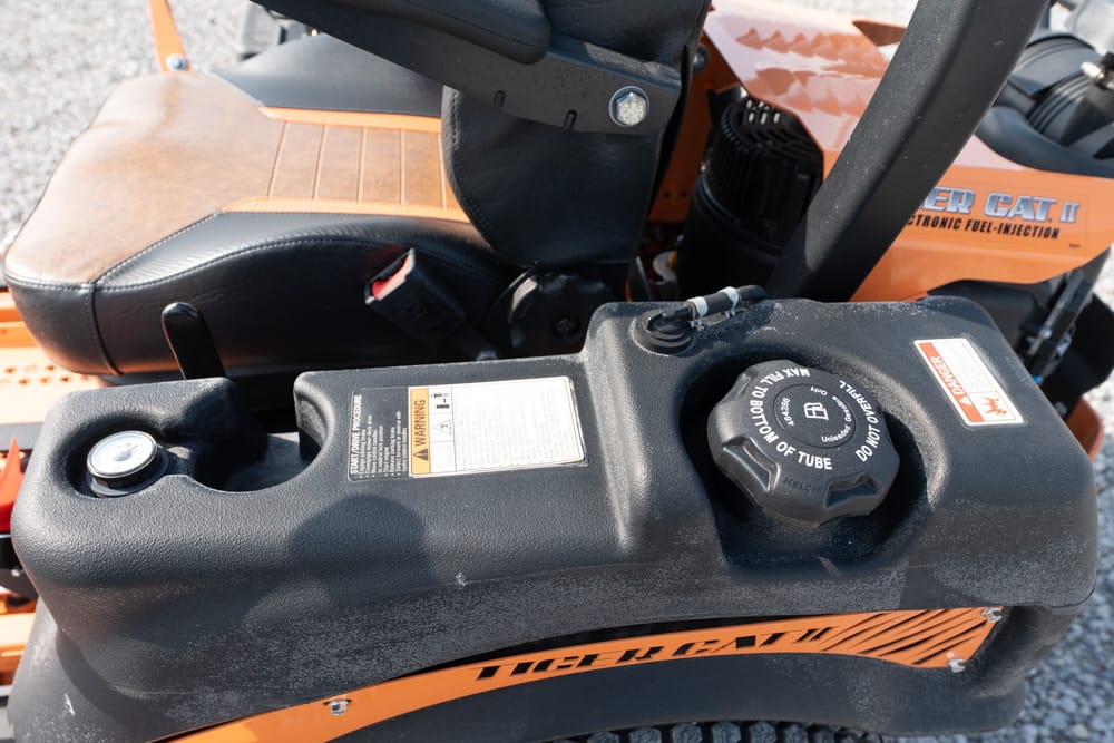 Close-up of the black fuel tank and fill cap on an orange riding mower, with a warning label nearby.