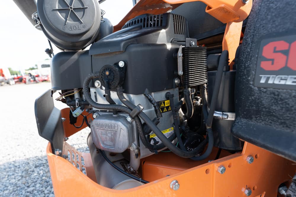 Close-up of an orange construction machine's diesel engine with exposed hoses and components in view.