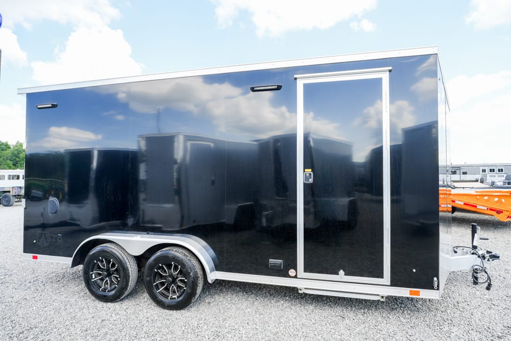 Black enclosed cargo trailer with tandem wheels and a side door on a gravel lot