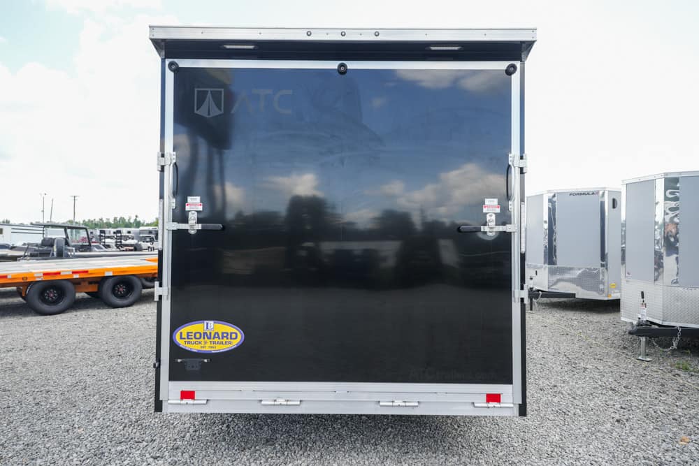 Back of a black enclosed cargo trailer with a Leonard trailer sticker, parked on a gravel lot.