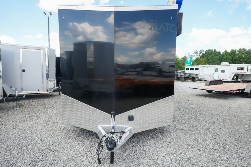 Black enclosed cargo trailer with diamond-plate front, hitched in a gravel lot with other trailers in the background.