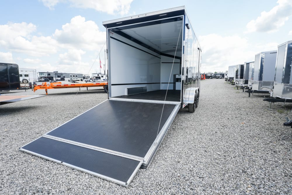 Open cargo trailer with a lowered ramp in a gravel lot, surrounded by other trailers in a storage yard.