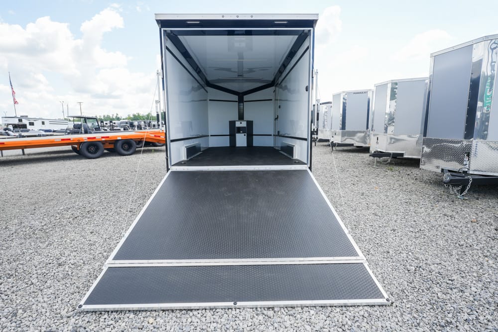 Open cargo trailer with lowered ramp in a gravel lot, interior empty and bright.