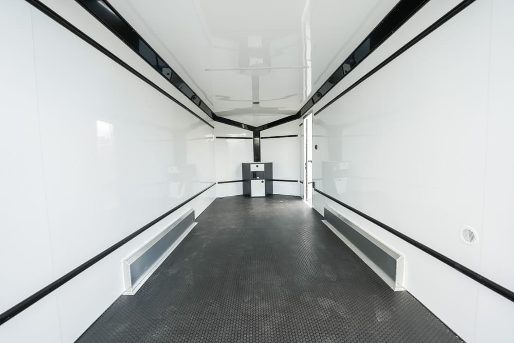 Empty white trailer interior with black trim and a small cabinet at the far end, viewed down the length of the space.