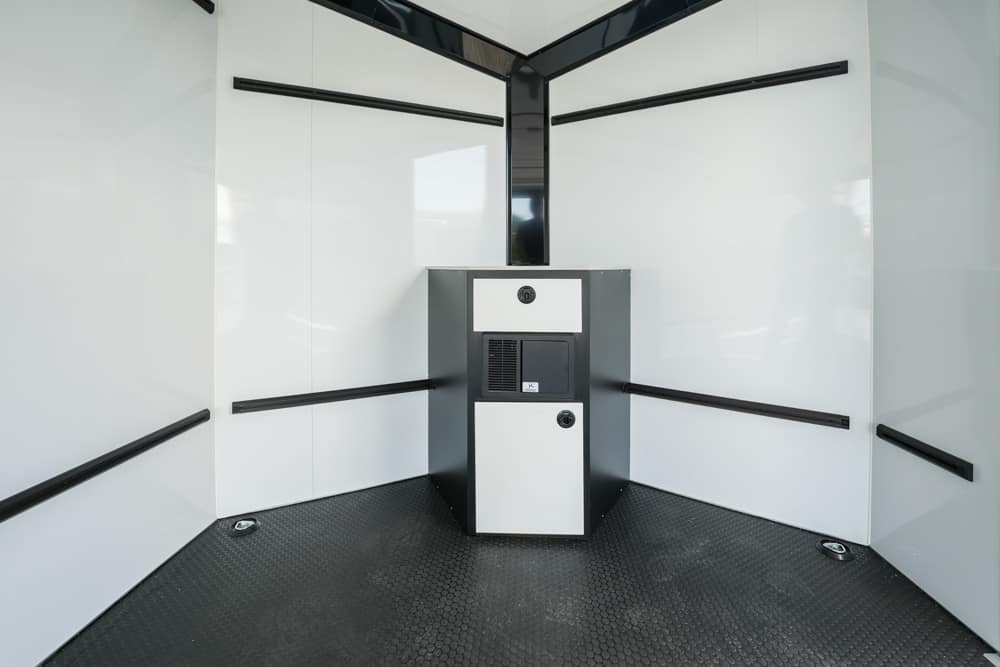 Small service chamber interior with white glossy walls, black wall rails, and a central gray control cabinet on a textured dark floor.