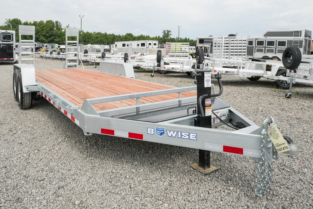 Flatbed trailer with a wooden deck in a gravel lot, surrounded by other trailers.