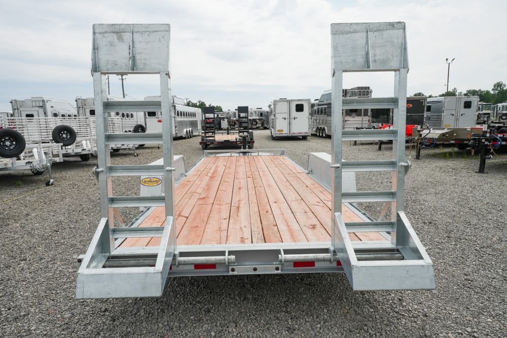 Flatbed trailer with wooden deck and dual loading ramps raised on both sides in a gravel trailer yard