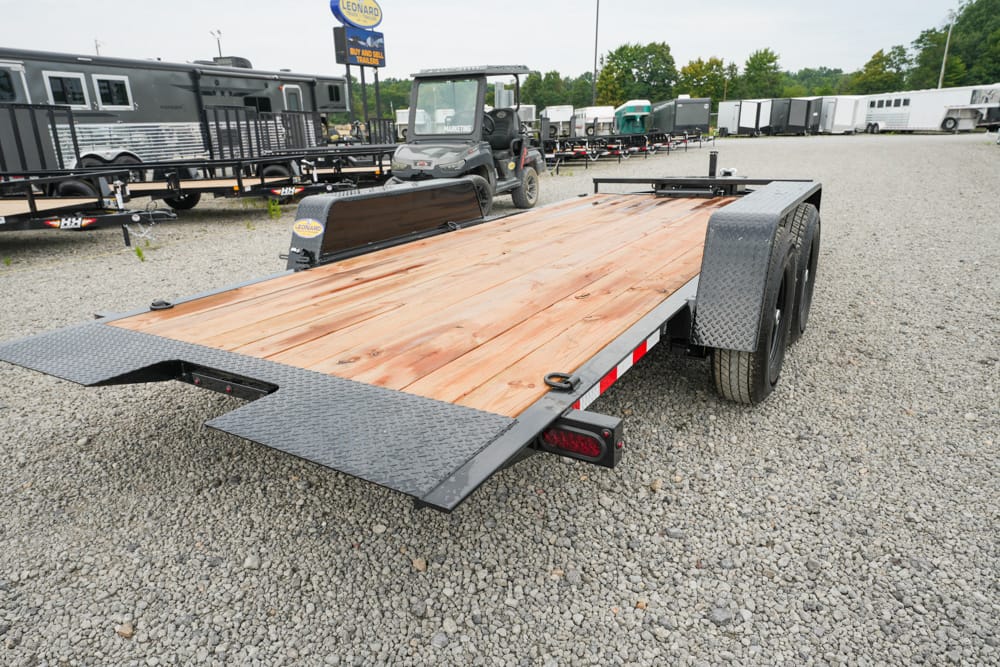 Flatbed utility trailer with a wooden deck and diamond-plate fenders on dual axles, parked on a gravel lot.