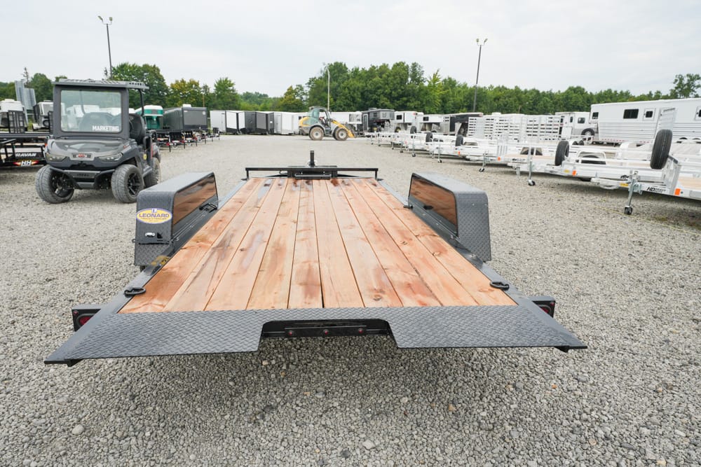 Flatbed trailer with a wooden deck parked in a yard full of trailers at a dealership or storage lot.
